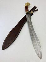 Full view of the Damascus steel sword next to its brown stitched leather sheath.