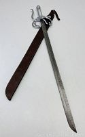 Full view of sword and brown leather sheath laid side by side on white background