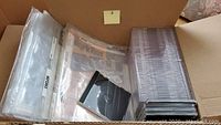 A box containing multiple clear CD and DVD cases and archival preserver sheets and negative preservers.