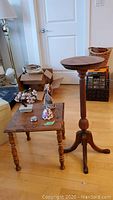 Wooden round plant stand and square side table on wooden floor with some boxes and background door