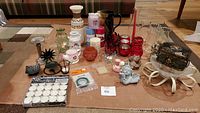 View of entire assortment on cardboard surface showing assorted candles, candle holders, vases, trinket box, cherubs, and floral accessories