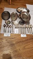 Photo of all items arranged on floor showing tarnished condition of trays, spoons, forks, coasters, and tongs