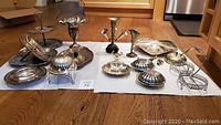 Full view of 14 silverplated and metal items arranged on the floor, including two-tiered trays, vases, trays, and serving ware.