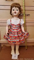 Front view of 29-inch tall vintage Pedigree doll wearing original colorful dress, standing against wooden background with measuring tape showing height.