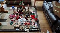 Wide shot showing all collected Christmas decorations spread out on carpet including tree, wreath, ornaments, bead garlands, candles, and craft supplies.