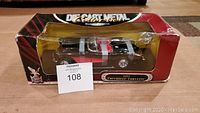 Side view of boxed diecast metal Chevrolet Corvette model car showing black and red paint with silver stripes and detailed wheels.
