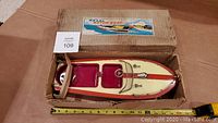 Top view of the metal model motor boat inside original box with measuring tape to show length near 16 inches.