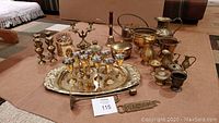 Full set of brass items including teapot, goblets, tray, vases, bucket, pitchers, cauldron, bell, candleholders, trinket bowl arranged on carpet