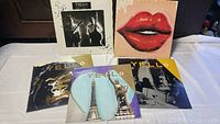 Front view of five Yello vinyl records layed out, showing album cover artwork including lips and landmarks