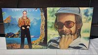 Front covers of two Elton John vinyl albums, "Caribou" and "Face to Face"