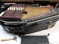 Chromaharp chromatic zither in case showing wooden soundboard, strings, tuning pegs, and buttons.