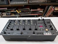 Front angle of Pioneer DJM-3000 DJ mixer placed on a table with vintage audio equipment in the background.