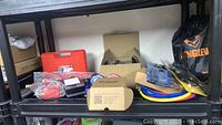 Shelf view showing various packaged tools including hoses, gauges, snake drain bag, and tool cases.