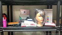 Photo showing assorted beauty items on shelf including mannequin head, boxes, and a hair dryer