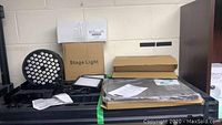 Overview of lot including multiple stage lights, boxes labeled Stage Light and tablet/laptop holder boxes, instruction manuals, and cables.