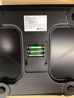 Underside view of one Renpho smart scale showing battery compartment with 3 AAA batteries and product specifications label.