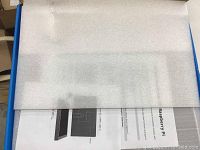 Photo of the monitor box with packing material and instruction manual visible under packaging foam.