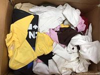 Box filled with assorted short sleeve shirts in various colors and patterns, mostly lightweight fabric, some with tags.
