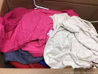 Pile of various colored hooded sweaters including bright pink, gray, and blue folded inside a box.