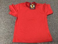 Plain red short sleeve shirt lying flat on carpet