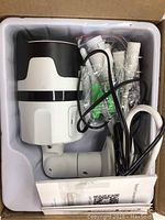 White and black smart security camera in box with mounting parts and cables visible