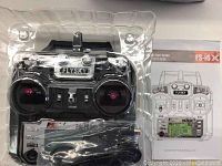 Black FlySky FS-i6X 6-channel digital proportional radio control transmitter in plastic packaging with Quick Start Guide manual underneath.