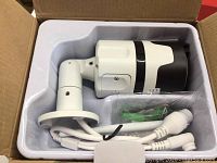 Smart security camera in original packaging showing the camera and mounting hardware inside a white plastic tray within a cardboard box.