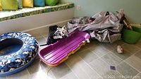 Photo showing LL Bean fabric covered inner tube sled with blue and black camouflage fabric cover, purple plastic sled with yellow edges, and white adjustable snowshoes.