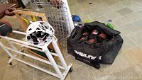 Photo showing metal sports ball cart with white Xenith football helmet placed on it, and black Rawlings sports bag on the floor with footballs inside.
