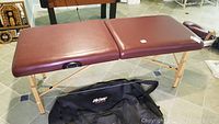 Full view of the LifeGear folding massage table set up with brown faux leather padded surface and wooden legs, with carrying bag underneath.