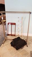 Metal clothing rack frame with wire shelf and black garment bag on floor plus wooden cap and hat racks leaning against wall