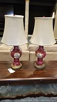 Two matching ceramic and brass table lamps with fabric shades, shown side by side on a wooden table.