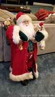 Full view of Santa Claus figure dressed in red coat with white fur trim, holding teddy bears in arms, standing upright