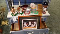 Photo showing sports-themed decor and memorabilia arranged on a surface and in an open drawer including candles shaped as sports balls, football dish, Patriots helmet, baseball bowls, a bat-shaped dish, David Ortiz bobblehead (missing one arm), party favors, and a framed print.
