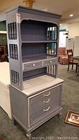Full view of wooden Dixie bedroom hutch painted grayish-blue with white trim, showing shelves, drawers and decorative spindle side panels.