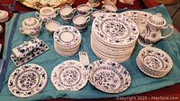 Photo showing full dinnerware set including teapot, plates, bowls, cups, creamer, sugar, butter dish, and serving platter spread on a cloth.