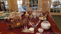 Wide view of table displaying multiple glassware, ceramic pieces including vases, glass figurines, and a metal Cinderella carriage candle holder to show full scope of items.