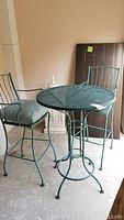 Front view of green metal mesh table with two matching chairs and cushions