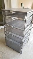 Front view of Elfa metal storage rack showing five mesh bins fixed in metal frame.
