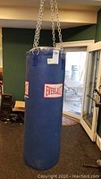 Full view of the blue Everlast punching bag hanging from heavy chain links indoors.
