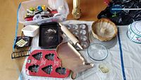 Full lot view showing cupcake pans, rolling pin, USA-shaped cake pan, Christmas cake mold, glass mixing bowl and loaf pan, corn basket, thermometers in plastic container, cake knives, flatware, and more.