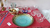 Image showing variety of crystal and cut glass bowls including colored centerpiece and clear glass pieces on a red cloth with other glassware nearby.