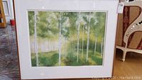Framed painting showing full birch tree forest scene in green hues, mounted on easel or floor