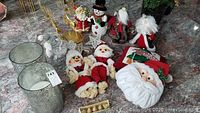 Two images showing the variety of Christmas figures, Santas, metal star tree toppers, reindeer card holders, snowmen, mercury glass candle holders, and a Santa face decoration on a marbled surface.