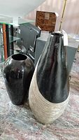 Two large ceramic vases placed on floor; one vase is glossy black and rounded, the other is taller with a black and beige spiral textured design.