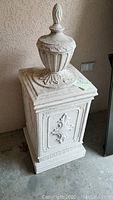 Front view of the faux cement decorative receptacle showing intricate molded designs and finial-topped lid.