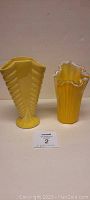 Pair of yellow glass vases on white surface against white wall, including Shawnee Ring Fan vase and swirl vase