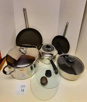 Photo showing all cookware items including soup pot, saucepans, skillets, and glass presses arranged on a surface.