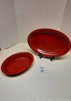 Photo of two red Fiestaware ceramic serving dishes on a white display surface with no stands included.
