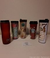 Front view of all five Starbucks travel mugs showing distinct colors and designs in a single row on table.